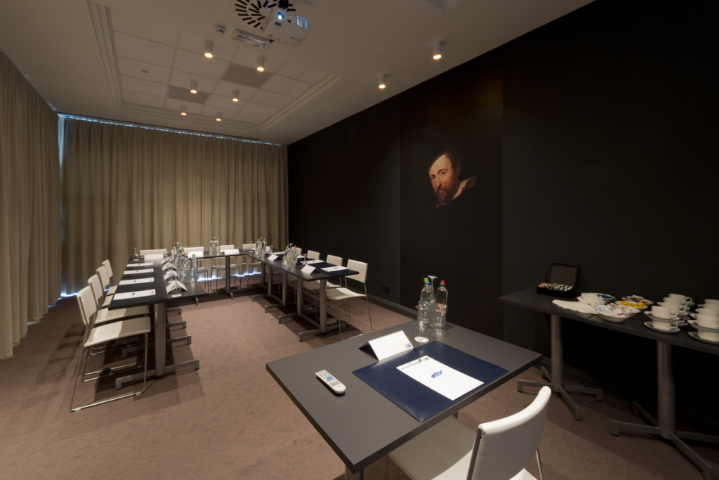 Der Veranstaltungsraum mit 17 Plätzen in u-förmiger Anordnung. Die Vorhänge sind zugezogen.